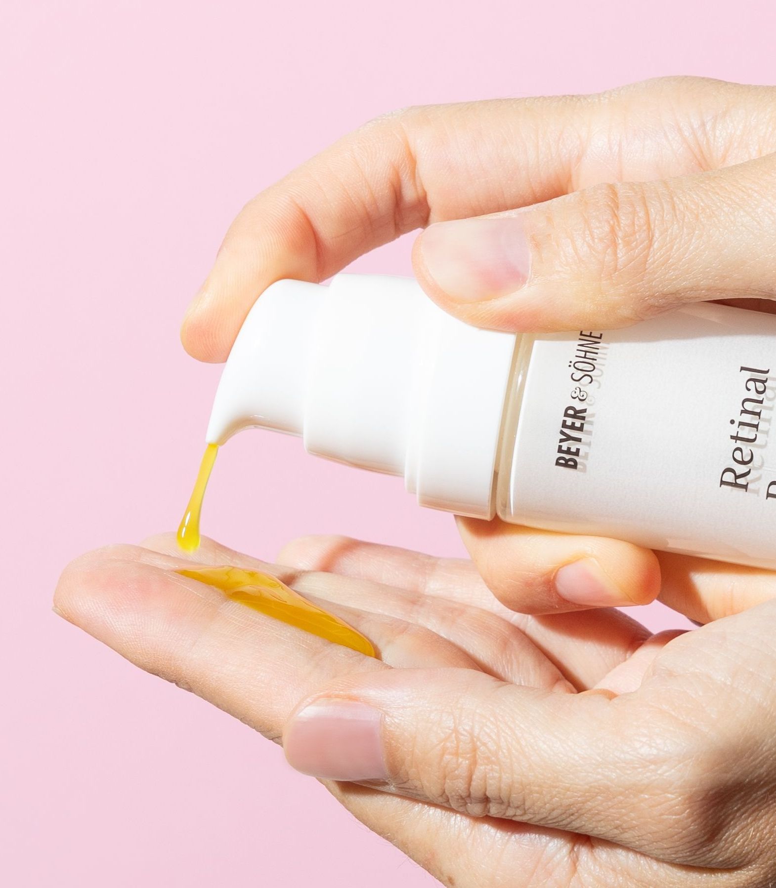 Hände, die ein Serum von Beyer & Söhne mit der Aufschrift Retinal Booster halten. Eine hellgelbe Textur wird auf zwei Finger aus dem Pumpspender gespritzt.